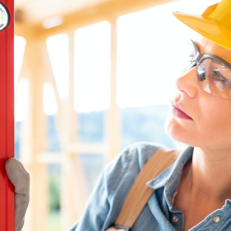 Woman worker at building site of wood frame house using level tools